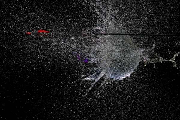 An arrow pierces a water balloon and creates a spectacular water spray explosion against a black background, high-speed shot, water balloon, arrow