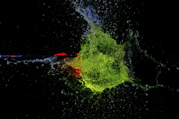 A green water balloon is pierced by an arrow and explodes in a dark, dynamic scene, high-speed shot, water balloon, arrow