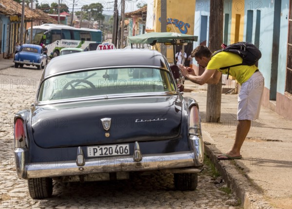 Tourist taking pictures in a vintage car at the roadside in the old town of Trinidad, Trinidad, Cuba, Sancti Spíritus, Cuba, Sancti Spíritus