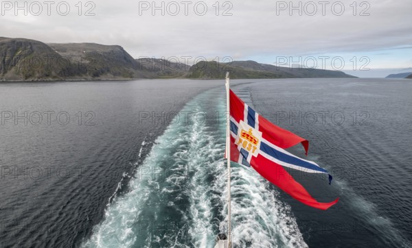 The post symbol on a Norwegian flag of a Hurtigruten ship, foaming spray, Honningsvåg, Finnmark, Norway, Scandinavia, Europe, adventure travel, fjord, flags, tourism, Honningsvåg, Hurtigruten, Hurtigruten trip, cruise, NOR, mail ship, travel, destination, sea trip, sightseeing, tourism, Norwegian, Norwegian flag, Scandinavian, touristic
