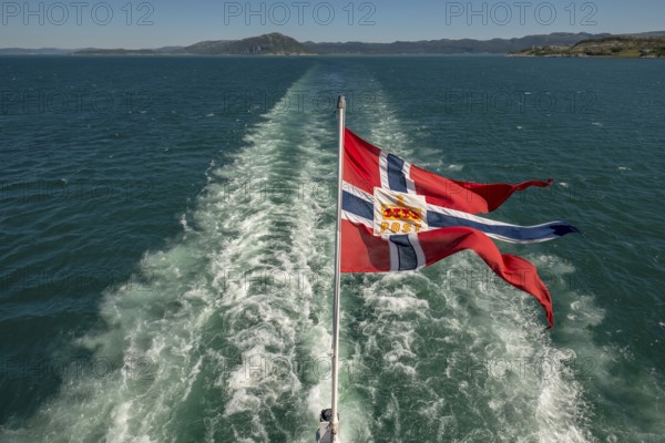 The post symbol on Norwegian flag of a Hurtigruten ship, foaming spray, Trondheimfjord, Agdenes, Trøndelag, Norway, Scandinavia, Europe, adventure trip, fjord, flags, tourism, Hurtigruten, Hurtigruten trip, cruise, NOR, mail ship, travel, destination, sea trip, sightseeing, tourism, Trøndelag, Norwegian, Scandinavian, touristic