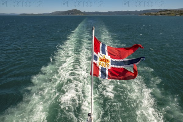 The post symbol on Norwegian flag of a Hurtigruten ship, foaming spray, Trondheimfjord, Agdenes, Trøndelag, Norway, Scandinavia, Europe, adventure trip, fjord, flags, tourism, Hurtigruten, Hurtigruten trip, cruise, NOR, mail ship, travel, destination, sea trip, sightseeing, tourism, Trøndelag, Norwegian, Scandinavian, touristic