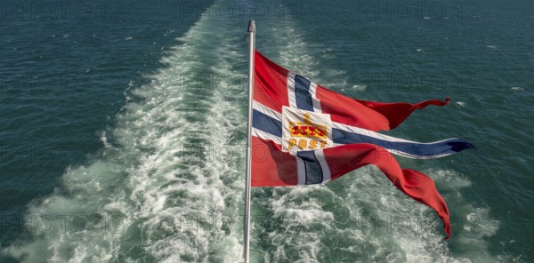 The post symbol on Norwegian flag of a Hurtigruten ship, foaming spray, Trondheimfjord, Agdenes, Trøndelag, Norway, Scandinavia, Europe, adventure trip, fjord, flags, tourism, Hurtigruten, Hurtigruten trip, cruise, NOR, mail ship, travel, destination, sea trip, sightseeing, tourism, Trøndelag, Norwegian, Scandinavian, touristic
