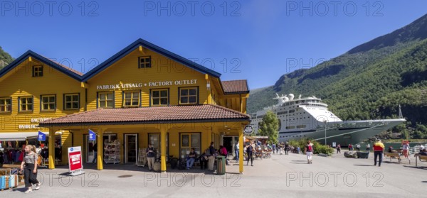 Tourists in Flåm, FABRIK KUTSALG FACTORY OUTLET, shops, yellow wooden house, excursion boat, fjord, mountain, trees, blue sky, Sogn og Fjordane, Norway, Scandinavia, Europe, Flåm, NOR, travel, tourism, destination, sightseeing, sea voyage, Hurtigruten, Hurtigruten trip, tourism, Norwegian, Scandinavian, tourist, cruise, adventure trip, pedestrian, river, forests, shipping, shops, shopping, shopping, signs, flags