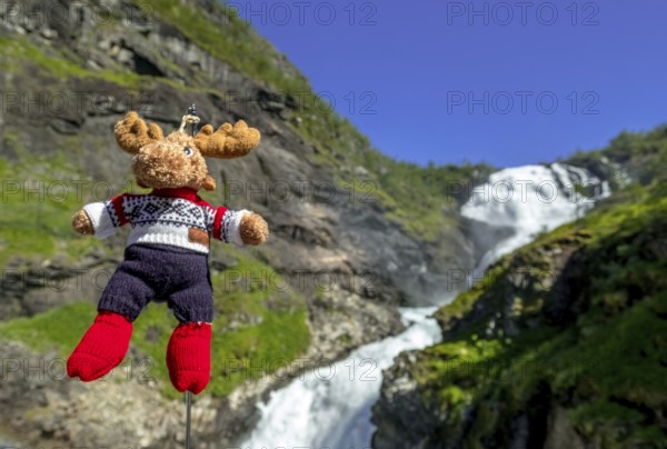Kjosfossen waterfall, mascot moose in front of waterfall, mountain, rock faces, meadow, sky, Fureberget, Flåm, Sogn og Fjordane, Norway, Scandinavia, Europe, Flåm, NOR, travel, tourism, destination, sightseeing, sea voyage, Hurtigruten, Hurtigruten trip, tourism, Norwegian, Scandinavian, tourist, cruise, adventure trip, waterfall, waters, trees, mountains, train journey, tour, travel by Flam Railway, Flam Railway