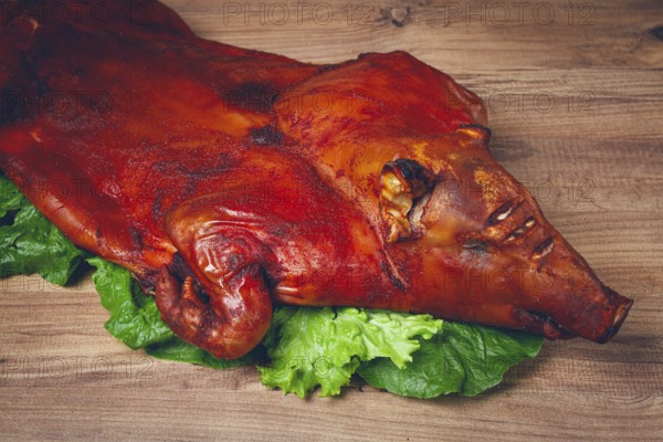 Baked, fried piglet, on a wooden table, no people, The whole piglet is baked and served on the leaves of a fresh green salad, showing off its crispy skin and detailed features
