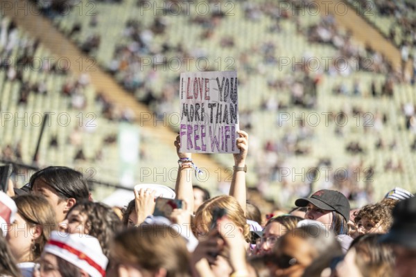 A festival visitor holds a sign I Love You More Than Free WiFi, Day 2 in the Olympic Park, Munich, 31/08/2025
