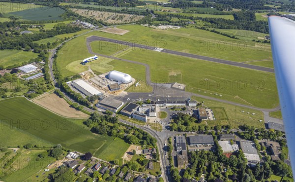 Aerial view, Essen/Mülheim Airport, Goodyear airship Zeppelin, construction site next to the WDL airship hangar, construction site and new office buildings with multi-storey car park (Pitstop centre), parked aircraft, runway and landing strip, Holthausen - Southeast, Mülheim an der Ruhr, Ruhr area, North Rhine-Westphalia, Germany, construction work, construction area, building site, building plots, construction project, construction site, DE, Europe, aerial view, aerial photography, aerial photography, overview, bird's-eye view, overview