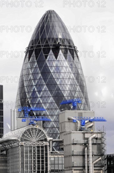 The Gherkin or Swiss-Re-Tower, in front of a historic building, London, England, Great Britain, Modern skyscraper with characteristic glass facade and cranes in the background, London, England, Great Britain
