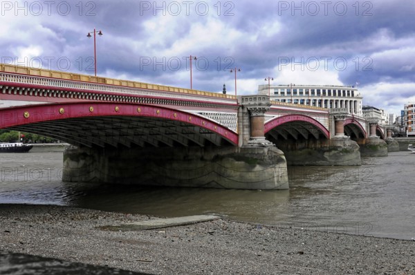 A pink bridge stretches across the Thames, with dense cloud cover above, London, England, United Kingdom