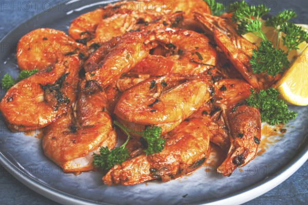 Fried white-footed shrimp, tiger prawns in a bowl, with lemon and herbs, on a blue background