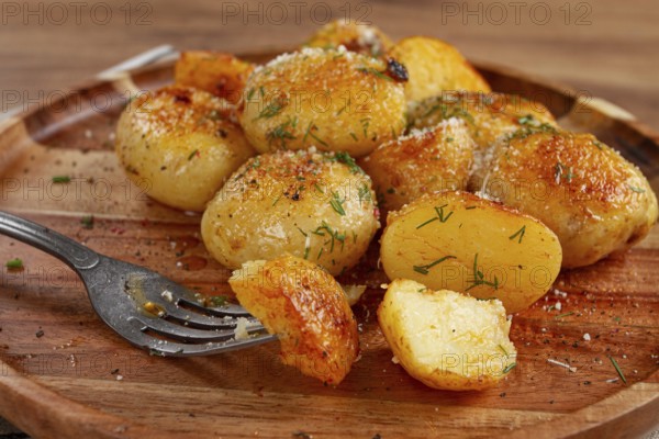 Half-eaten fried new potatoes, with butter and dill, on a wooden plate, with a fork, at home, without strangers