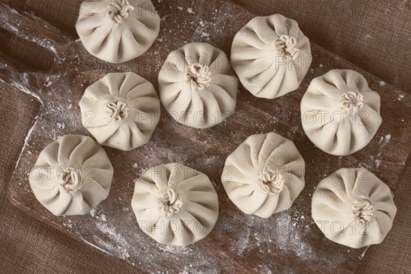 Freshly frozen khinkali, raw, on a wooden chopping board, top view, rustic style, no people