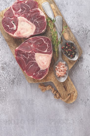 Freshly sliced beef legs, two ossobuco steaks, on a wooden board, with spices and herbs, ready to cook