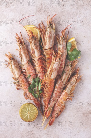 Shrimps on skewers, Grilled, spread on a marble surface, garnished, with lemon slices, and fresh herbs, view from above
