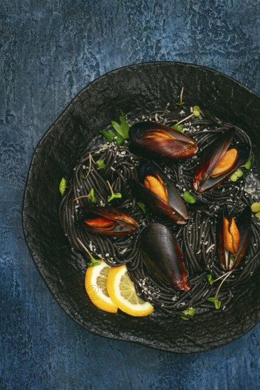 Spaghetti with black squid, black pasta, with boiled mussels, on a black plate, with parsley and parmesan cheese, close-up, selective focus, no people