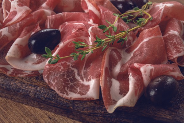 Freshly cut dried meat, served with olives and herbs, on a wooden chopping board, no people