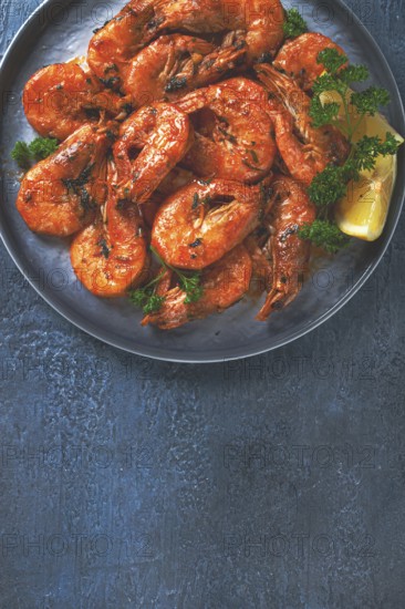 Fried white-footed shrimp, tiger prawns in a bowl, with lemon and herbs, on a blue background