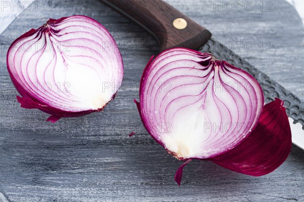 A vibrant red onion is cut in half, on a rustic wooden chopping board beside a sharp knife, ready for cooking