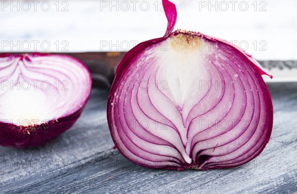 A vibrant red onion is cut in half, on a rustic wooden chopping board beside a sharp knife, ready for cooking