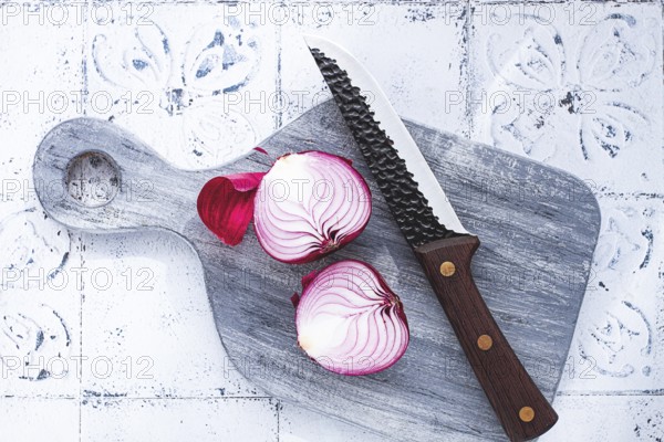 A vibrant red onion is cut in half, on a rustic wooden chopping board beside a sharp knife, ready for cooking