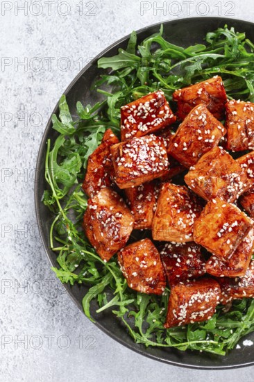 Fried salmon slices, teriyaki with sesame seeds, with arugula salad, top view