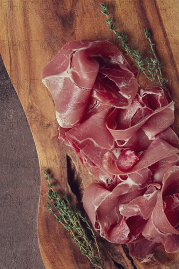 Slices of cured meat neatly arranged on a wooden board with fresh herbs in a rustic kitchen setting
