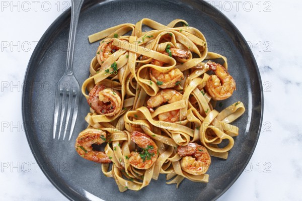 Fettuccine pasta with shrimp, spicy in soy sauce, on a grey plate with a fork, close-up