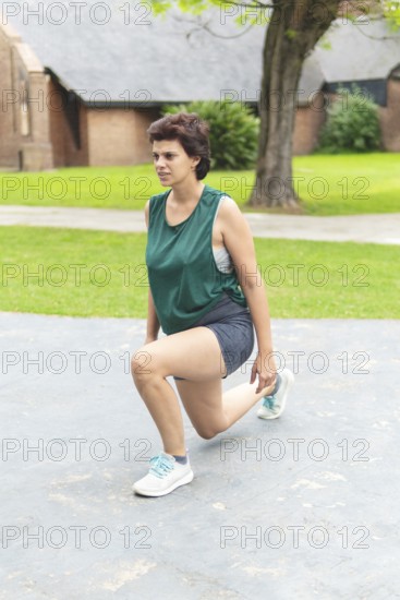 A focused woman performing a lunging stretch in a public park