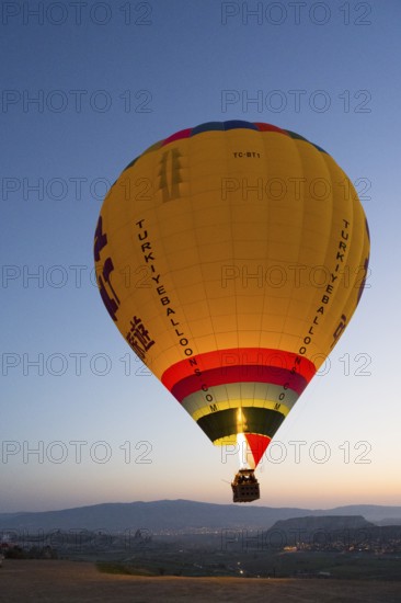 A large, luminous balloon floats over a clear mountainous landscape at dawn, Göreme National Park, Göreme Tarihî Millî Parki, Nevsehir Province, Nevsehir, Cappadocia, Cappadocia, Kapadokya, Cappadocia, Central Anatolia, Turkey