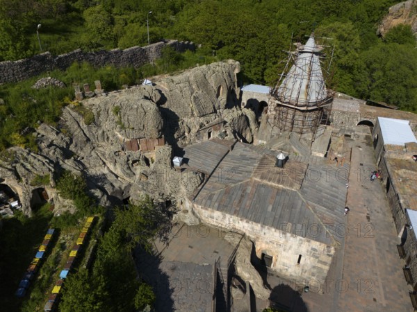 Old monastery in rocky landscape, surrounded by green nature, parts under renovation by scaffolding, aerial view, Geghard Monastery, UNESCO World Heritage Site, Kotayk Province, Armenia