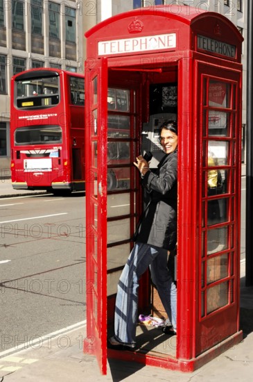 Red telephone box with smiling person and double-decker bus, London, London region, England, United Kingdom