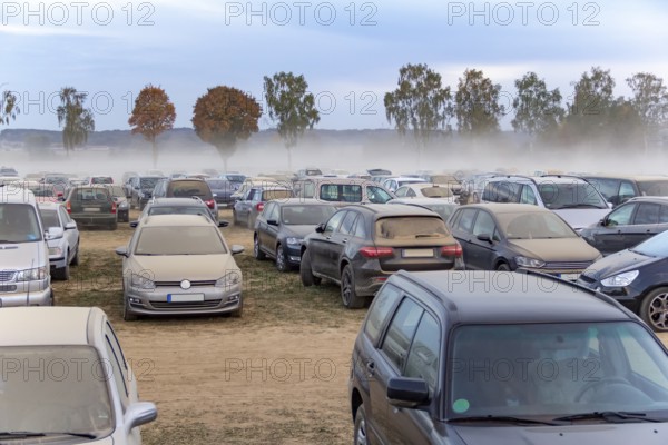 Dusty parking space scenery on a field including lots of dust covered cars at evening time in Southern Germany