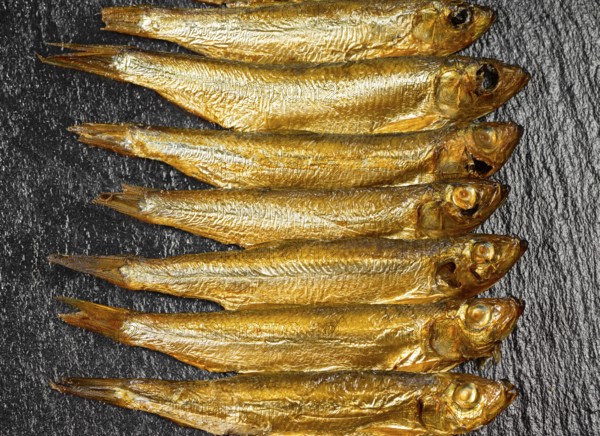 Arrangement with lots of fresh smoked sprats on dark stone slab