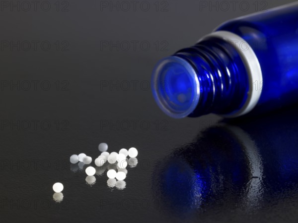 Detail of a open small blue bottle on dark reflective ground with globules around