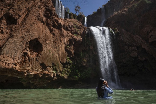 A Moroccan woman in swimsuit swimms under a waterfall Ouzoud in Morocco