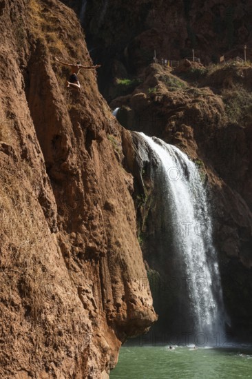 Moroccan young man jumps from the high rock into the water under a waterfall Ouzoud