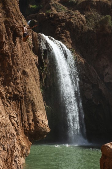 A Moroccan young man jumps from the high rock into the water under a waterfall Ouzoud