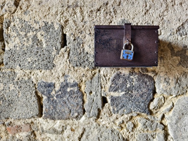 A metal box with a padlock hangs on a rough stone wall Styria Austria