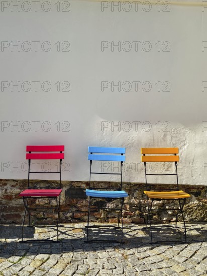 Three colourful chairs stand in front of a white wall on a paved floor Styria Austria