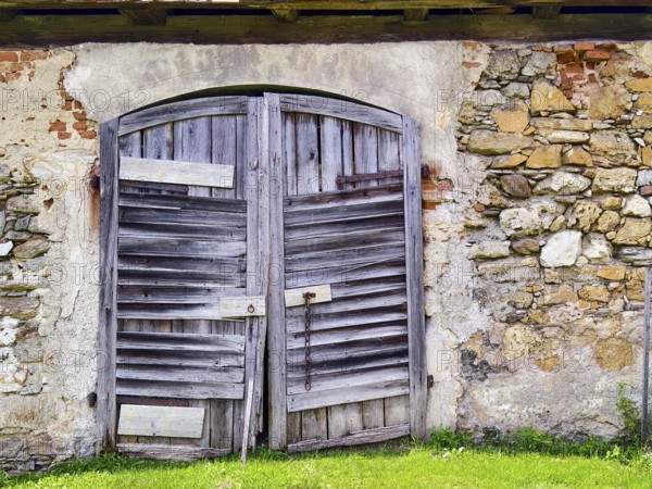 Large, weathered wooden gate in stone wall, emphasises rustic character Styria Austria