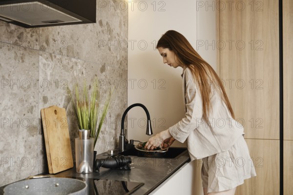 A woman with long hair is working at a stylish kitchen sink washing fresh vegetables