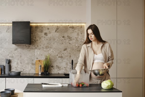 A pregnant woman is engaged in meal preparation in a contemporary kitchen. She sorts colorful vegetables while wearing comfortable clothing, highlighting a healthy lifestyle focus during the day