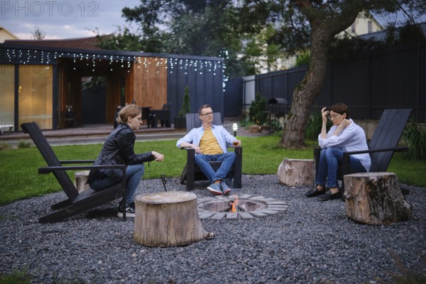 A family gather around a small fire pit in a backyard of tiny house, enjoying each their company. They share their thoughts and perspectives