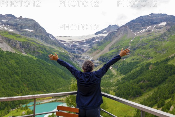 Woman with Arms Outstretched over the Beautiful Mountain Alp Grüm with Glacier and Alpine Lake Palü in the Swiss Alps in a Cloudy Summer Day in Poschiavo, Bernina, Grisons, Switzerland