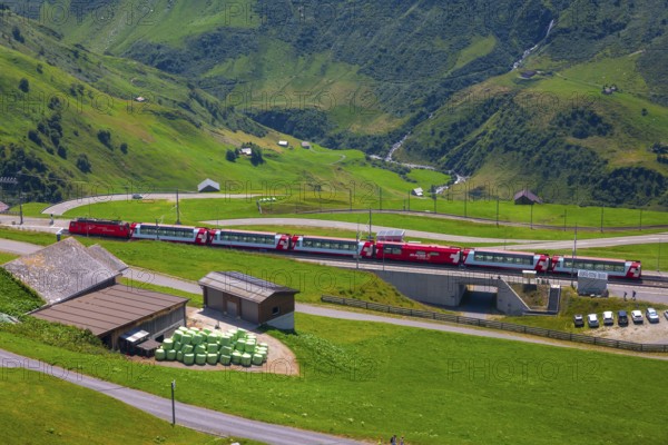 Beautiful View over Mountain Valley with Mountain Road and Railroad Station with Glacier Express Train in a Sunny Summer Day in the Swiss Alps in Andermatt, Uri, Switzerland