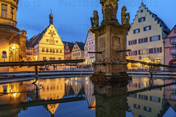 The market square with the Ratstrinkstube is reflected in the Georgsbrunnen fountain at dusk, Rothenburg ob der Tauber, Bavaria, Germany