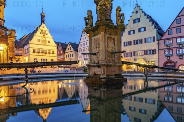 The market square with the Ratstrinkstube is reflected in the Georgsbrunnen fountain at dusk, Rothenburg ob der Tauber, Bavaria, Germany