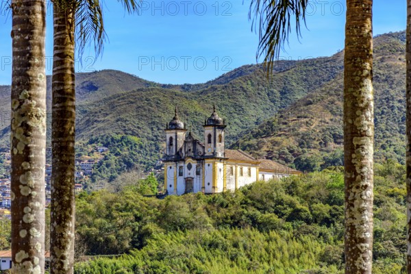 Hill with historic baroque church seen through the trees with the mountains of the city of Ouro Preto, Ouro Preto, Minas Gerais, Brazil
