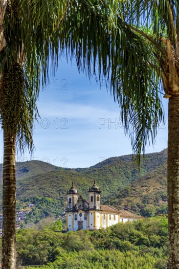 Historic baroque church seen through the trees with the mountains of Ouro Preto city, Ouro Preto, Minas Gerais, Brazil